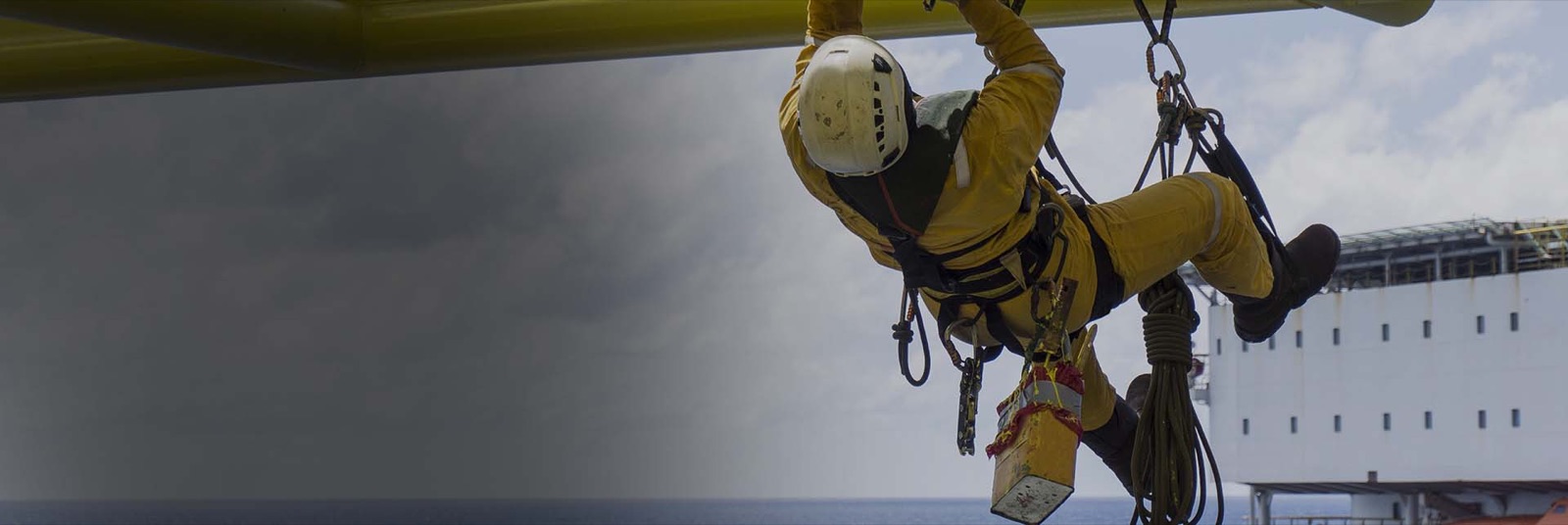 Rope access technician suspended on ropes beneath an offshore structure during maintenance work